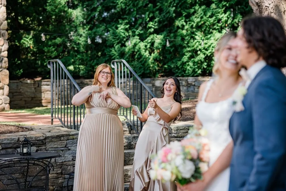 Bridesmaids watch as the bride sees the groom on the lawn by stone steps