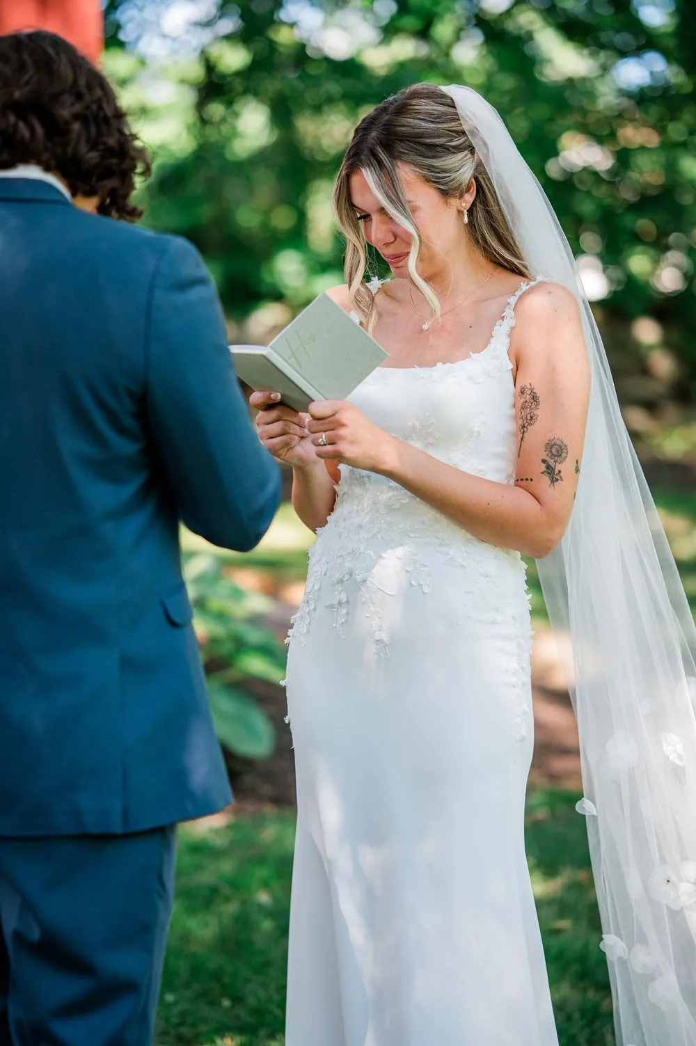 The bride reads private vows through tears from a small sage vow book