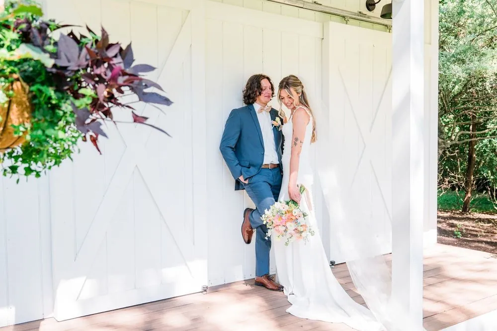 Fallon and Dom lean against white barn doors hung with a floral wreath