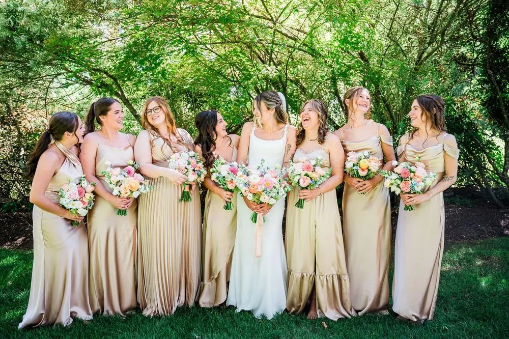 The bride with bridesmaids in champagne satin gowns under green trees