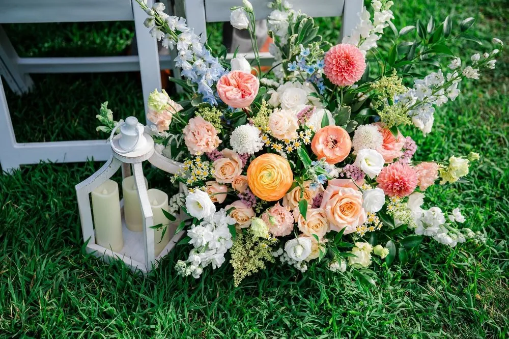 Peach, pink and cream flowers gathered at the base of the ceremony aisle