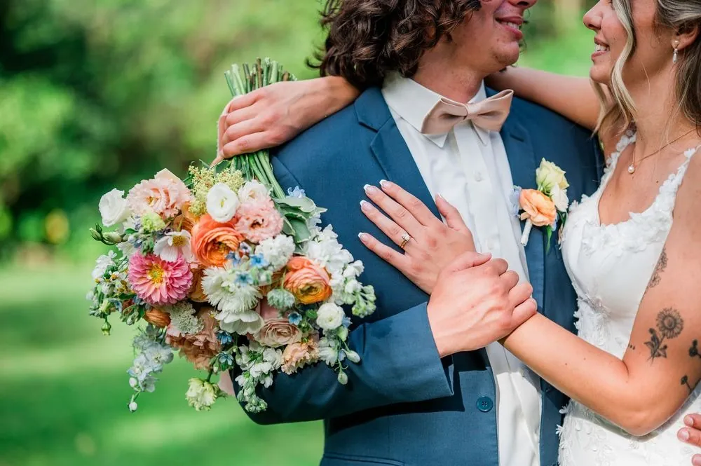 Close view of the couple embracing, her bouquet of peach roses on his shoulder
