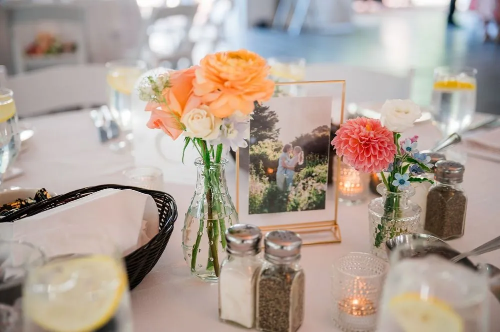 A reception table with peach flowers, candles and a framed photo inside the tent