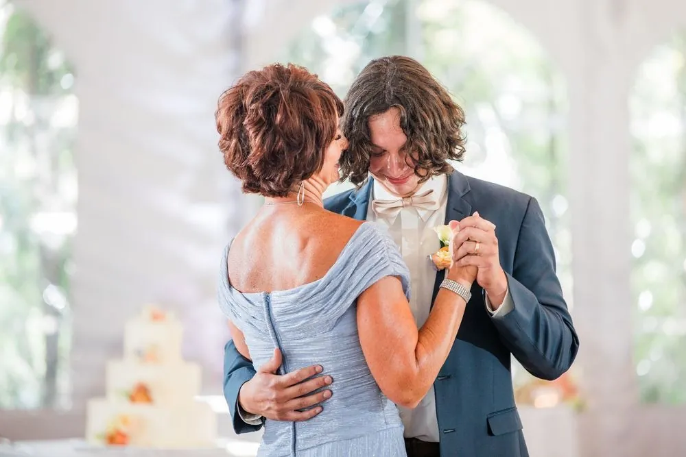 The groom dances with a woman in a pale blue dress beside the cake