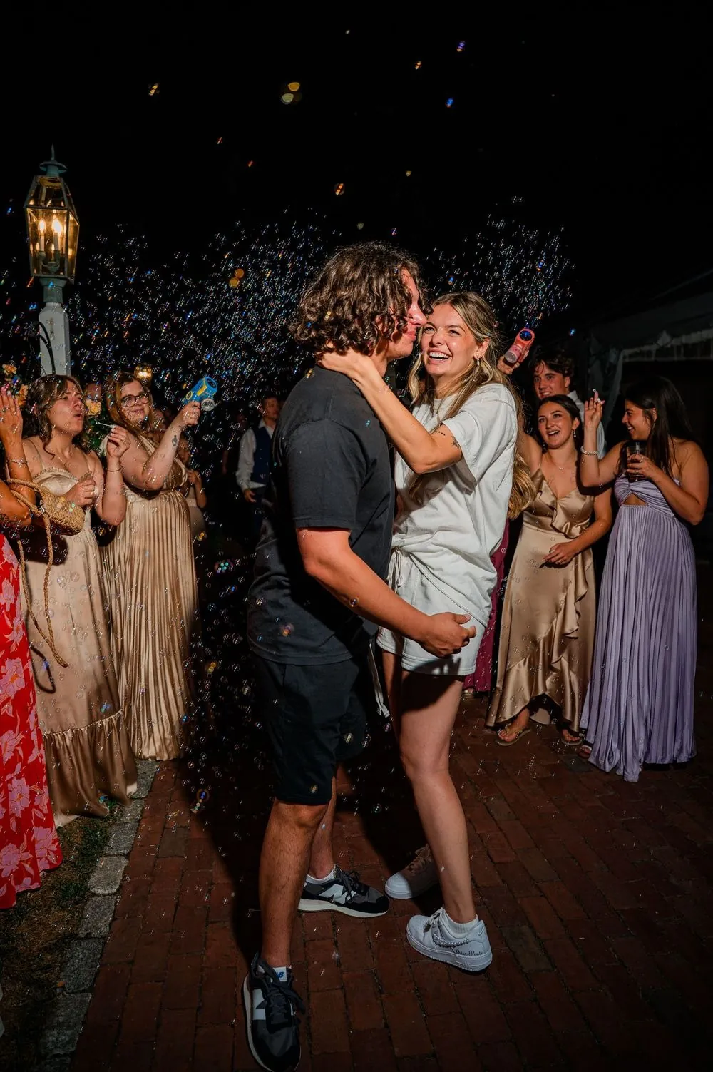 Fallon and Dom in t-shirts and sneakers embrace in a cloud of bubbles at night