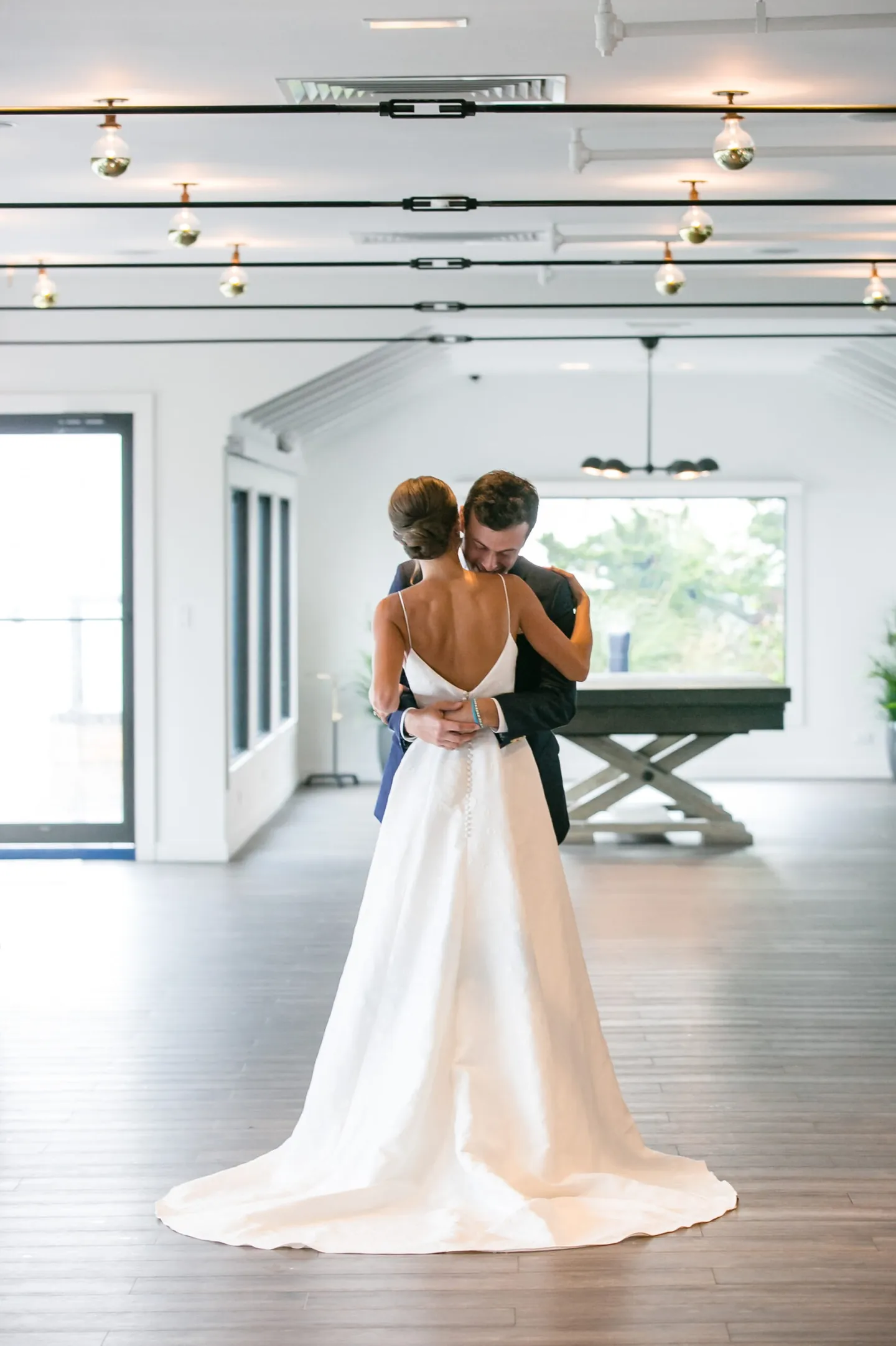 Hannah and Mark embrace alone in a bright empty room with white walls and wood floors