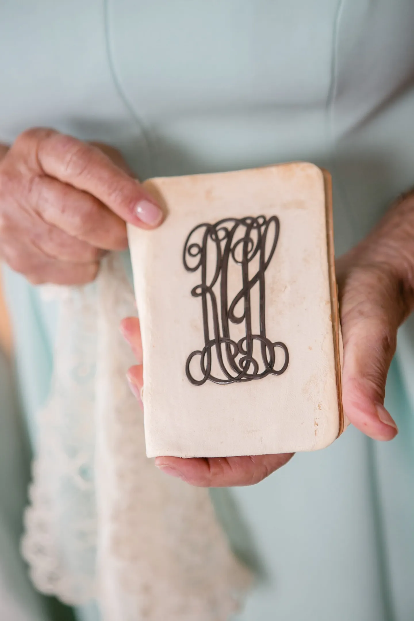 A hand holds a small square tile painted with an ornate navy monogram