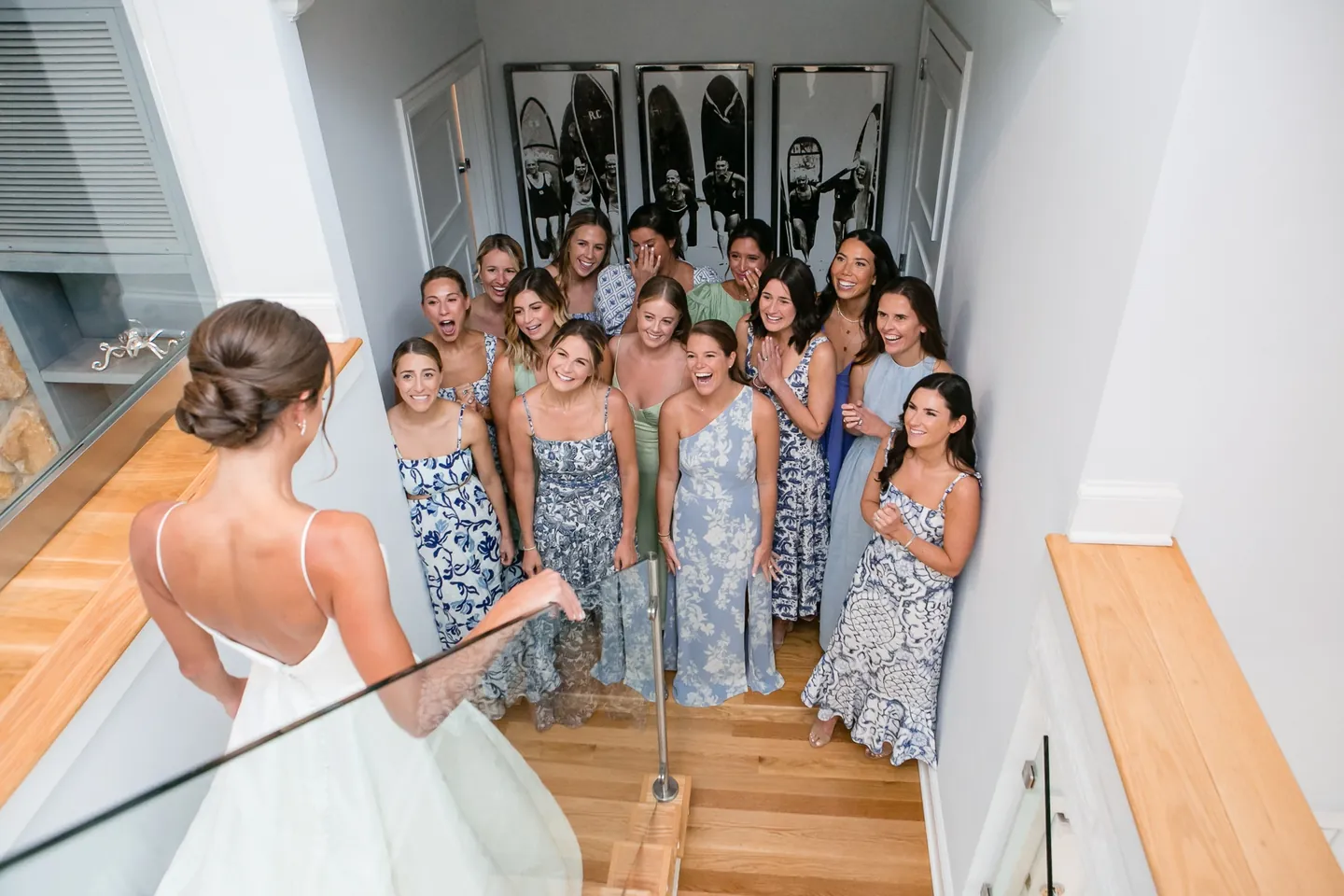 Bridesmaids in blue and green print dresses crowd a hallway reacting to the bride from behind