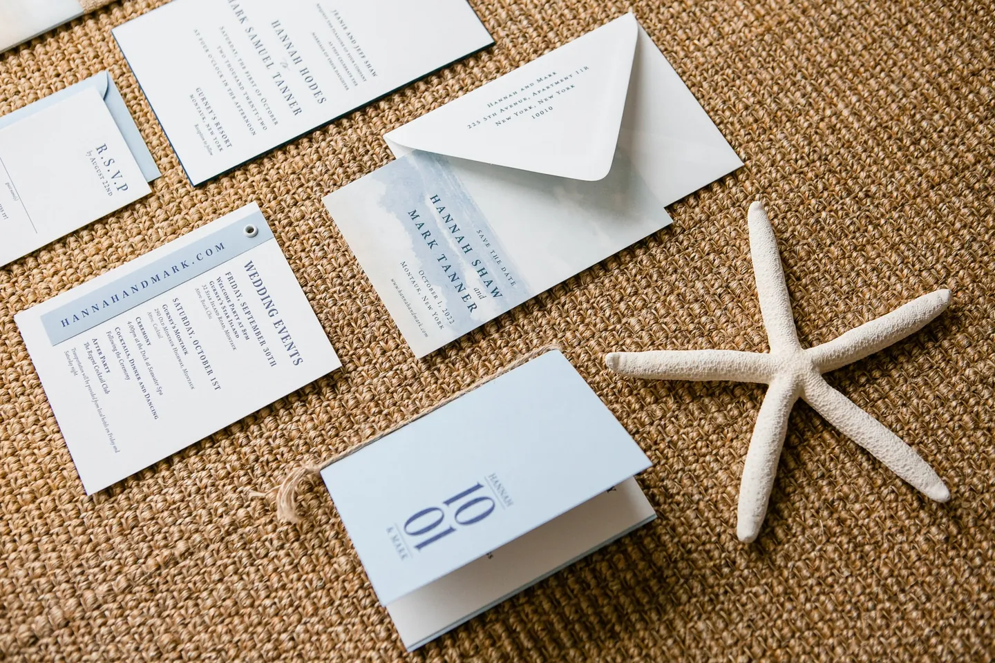 Pale blue invitation suite laid out on woven seagrass beside a dried starfish