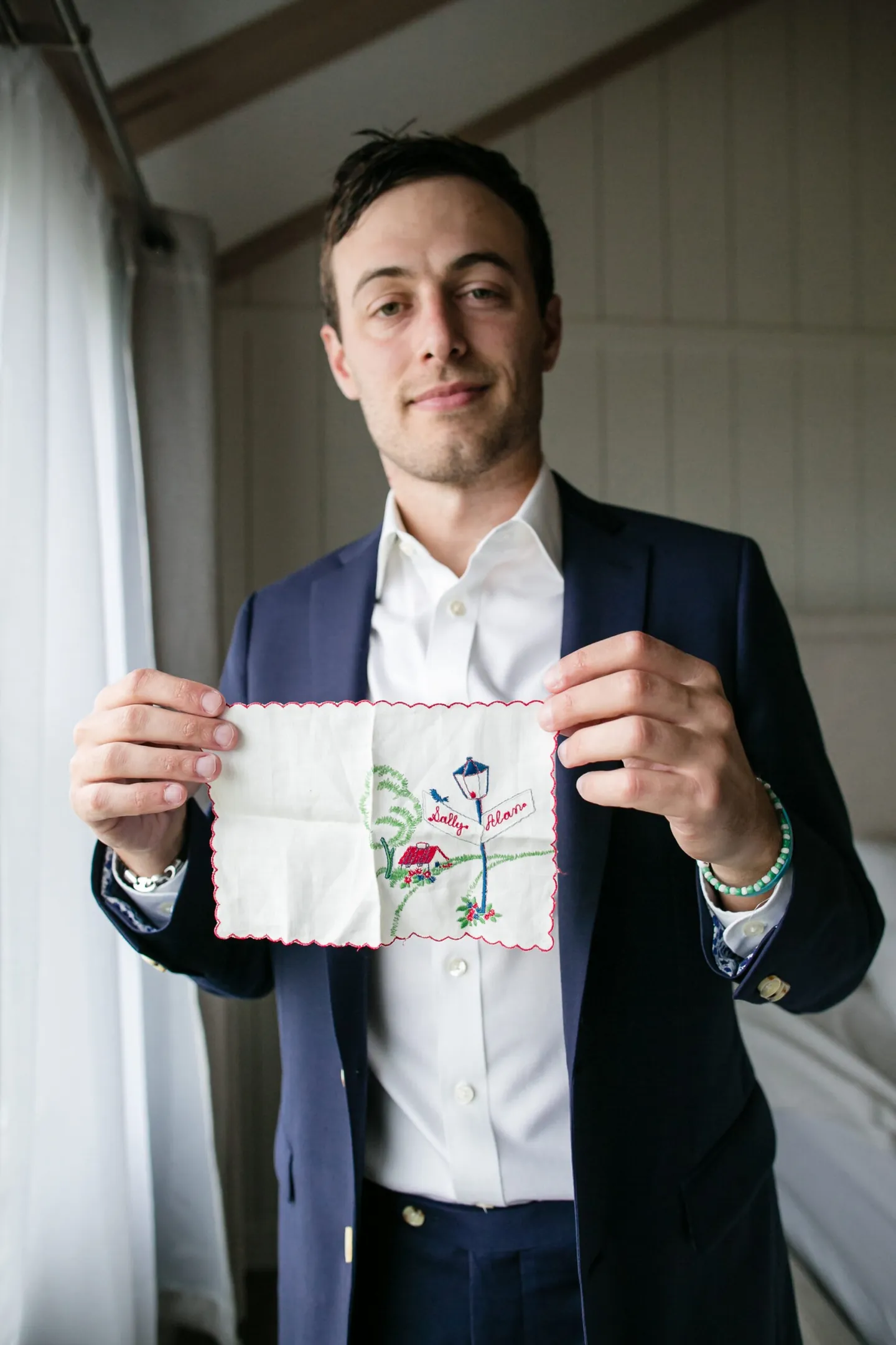 The groom in a navy suit reads a handmade card in a white room