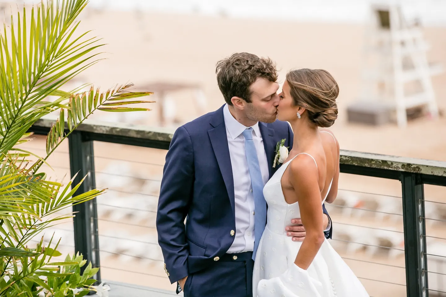 Mark kisses Hannah at the deck railing, palm fronds and an empty lifeguard chair behind