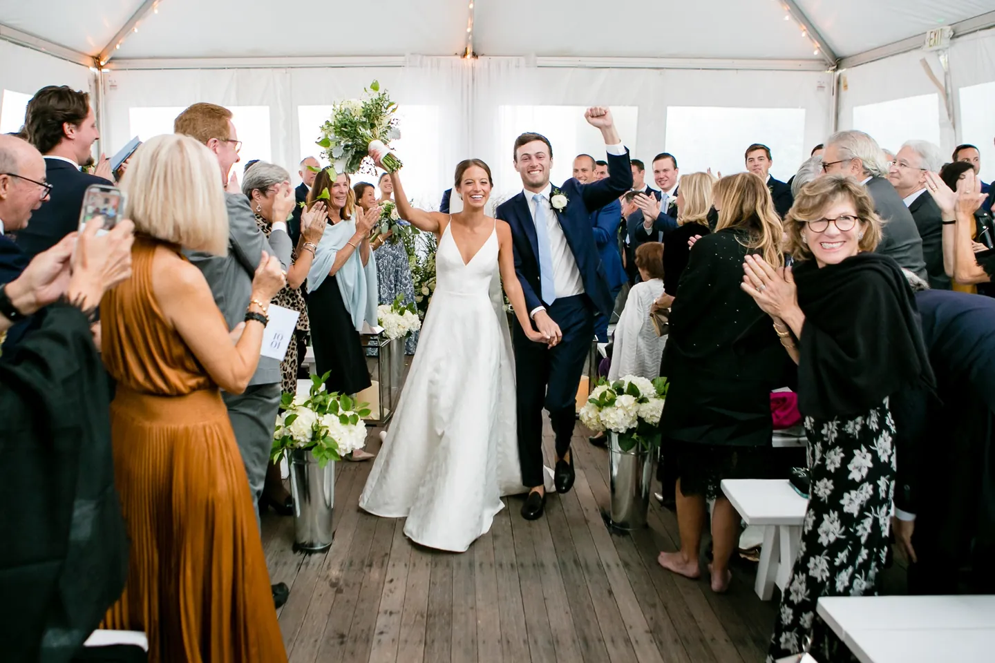 Mark pumps his fist and Hannah raises her bouquet walking back down the aisle past clapping guests