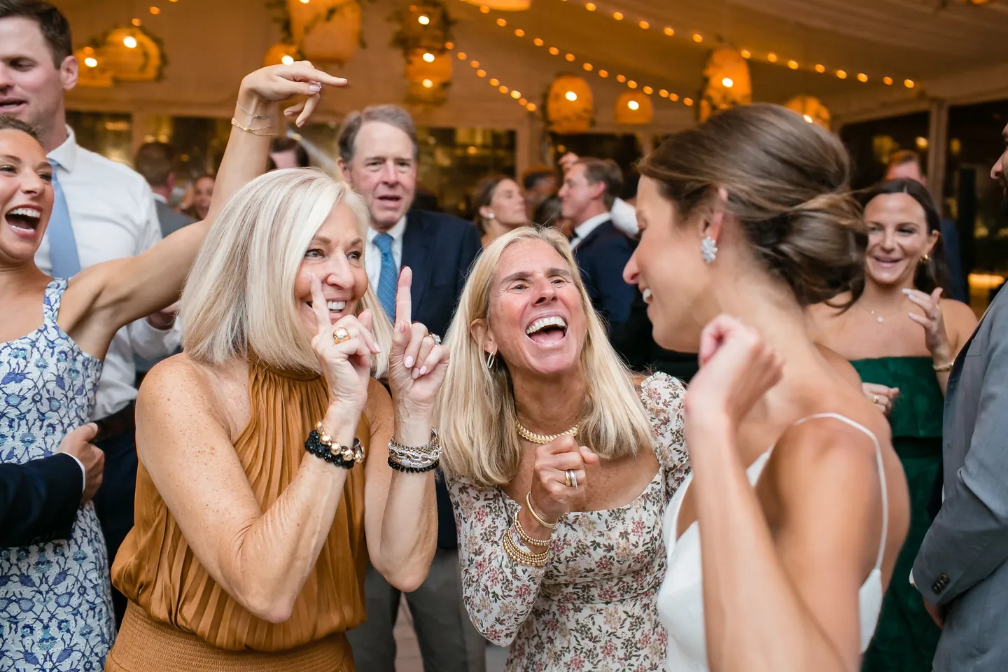 Women in bright dresses sing and laugh together on the packed dance floor
