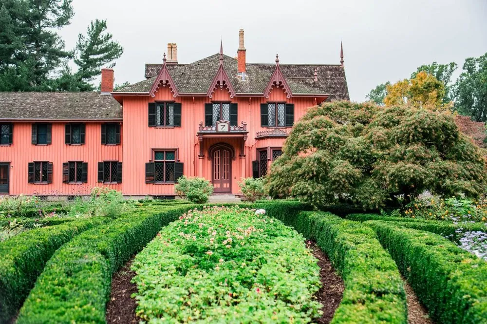 The pink Gothic Revival cottage behind a formal boxwood garden on an overcast day