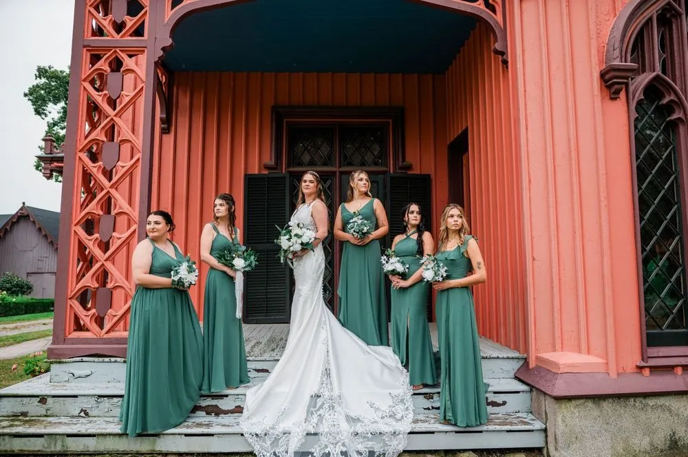 The bride stands with bridesmaids in sage gowns on the cottage's carved front steps