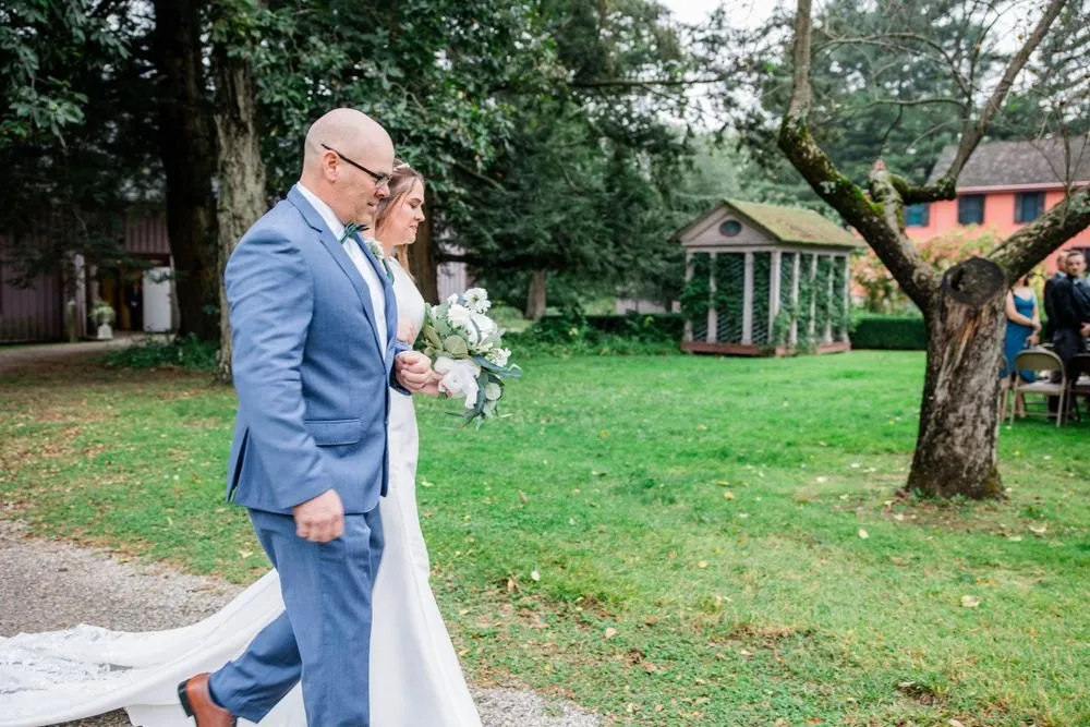 The bride's father walks her across the lawn toward the ceremony