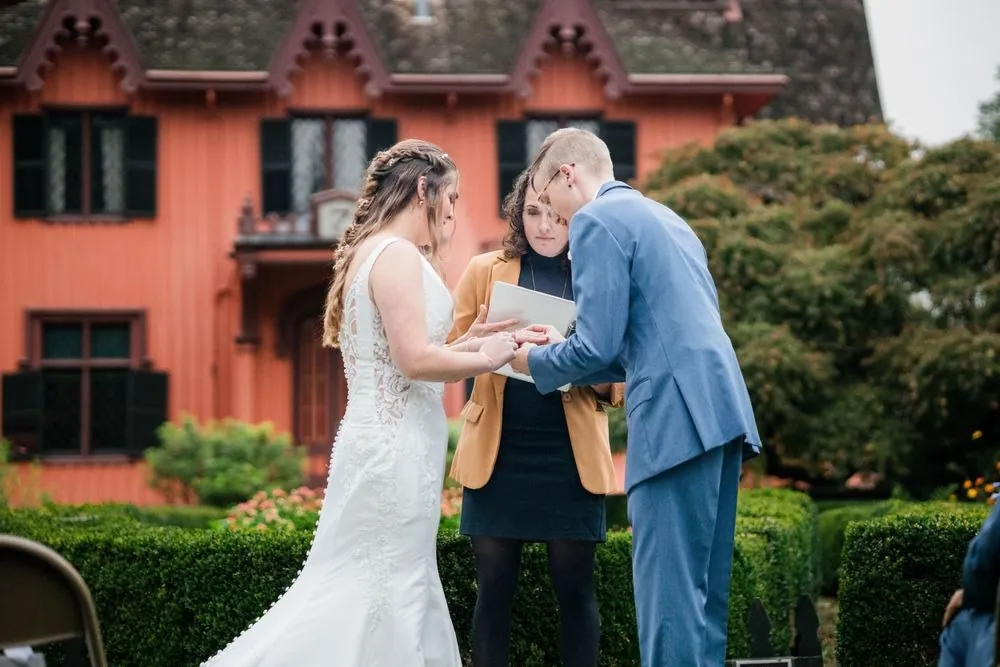The couple faces each other during the ceremony with the pink house behind them
