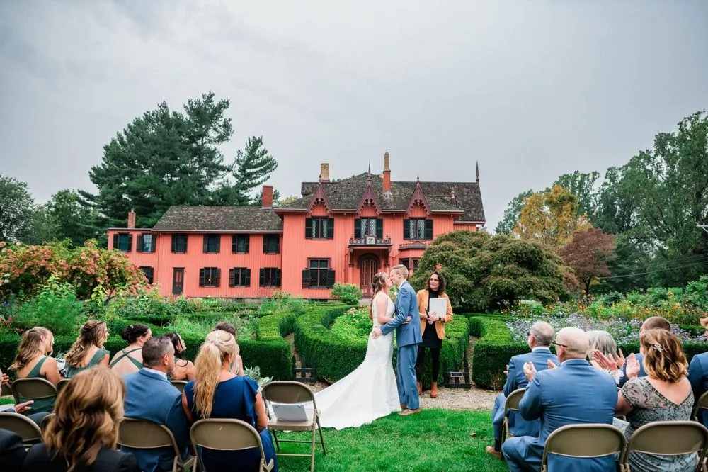 A wide view of guests seated on the lawn watching the ceremony before the cottage