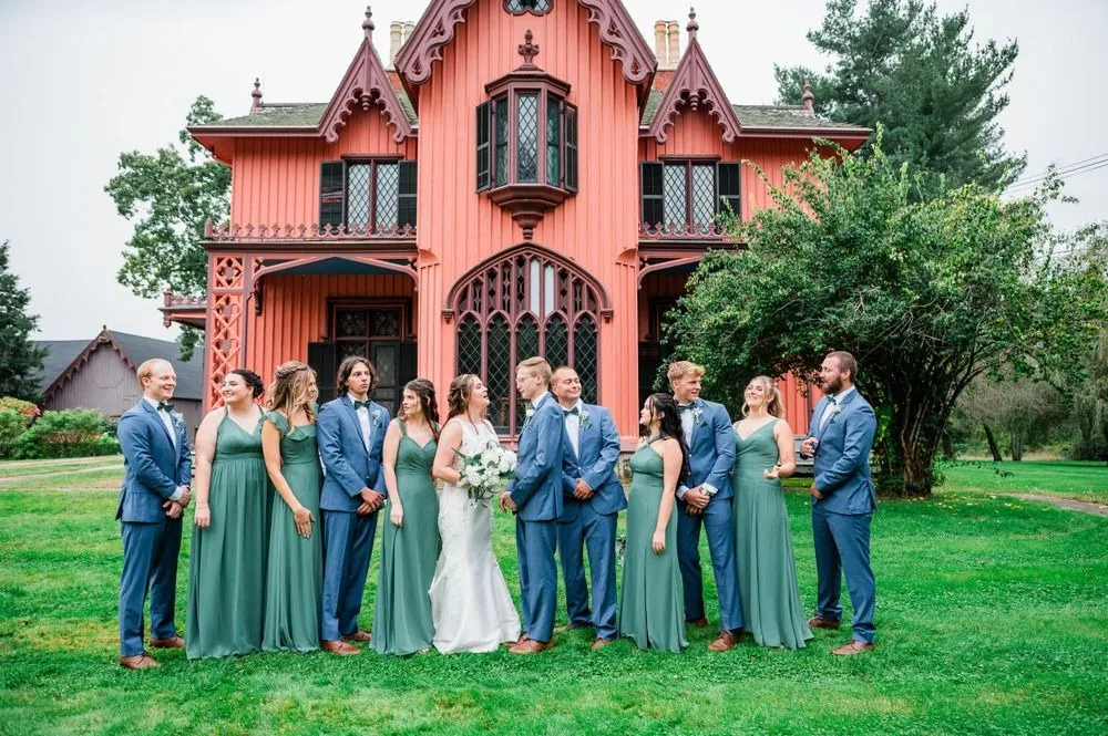 The full wedding party in sage and blue lined up in front of the pink cottage