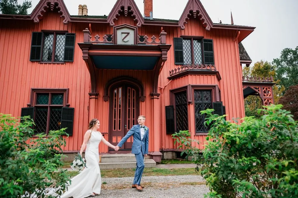 Hunter and Nick walk hand in hand past the carved front door of the pink cottage