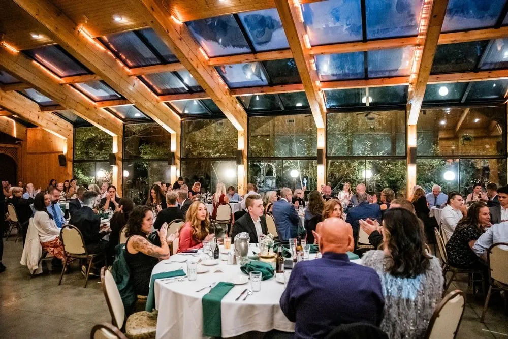 A wide view of the wood-beamed reception hall filled with guests at round tables