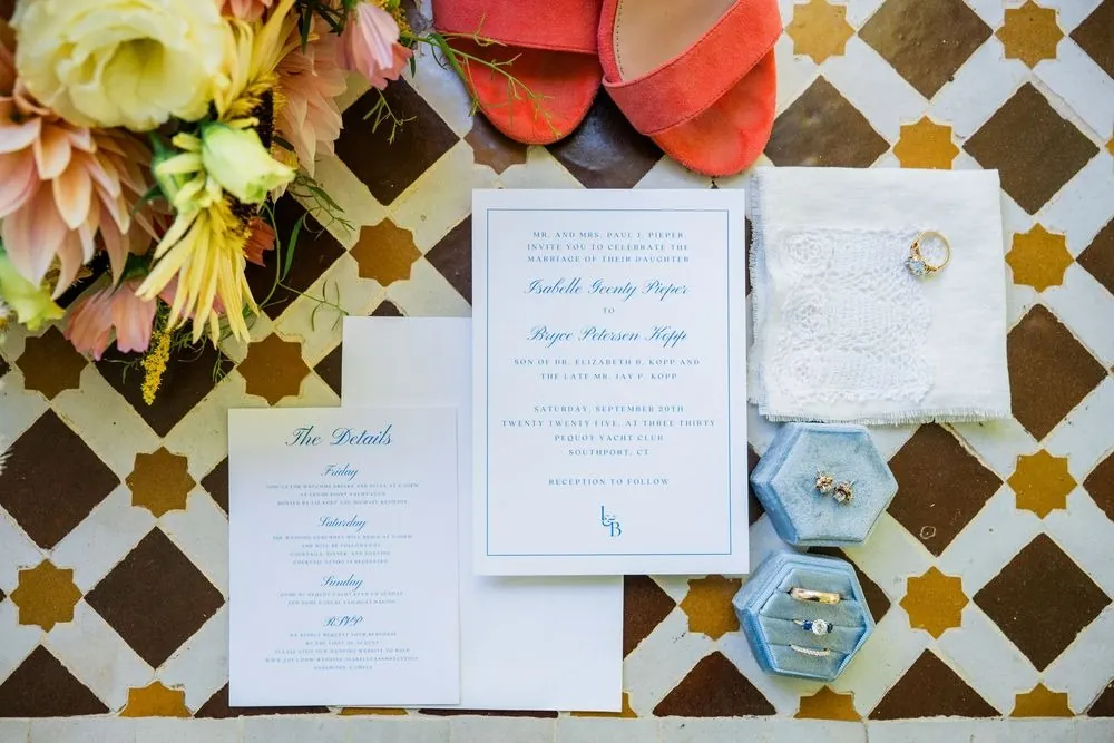Invitation suite, ring box, and bright florals laid out on a patterned tile floor