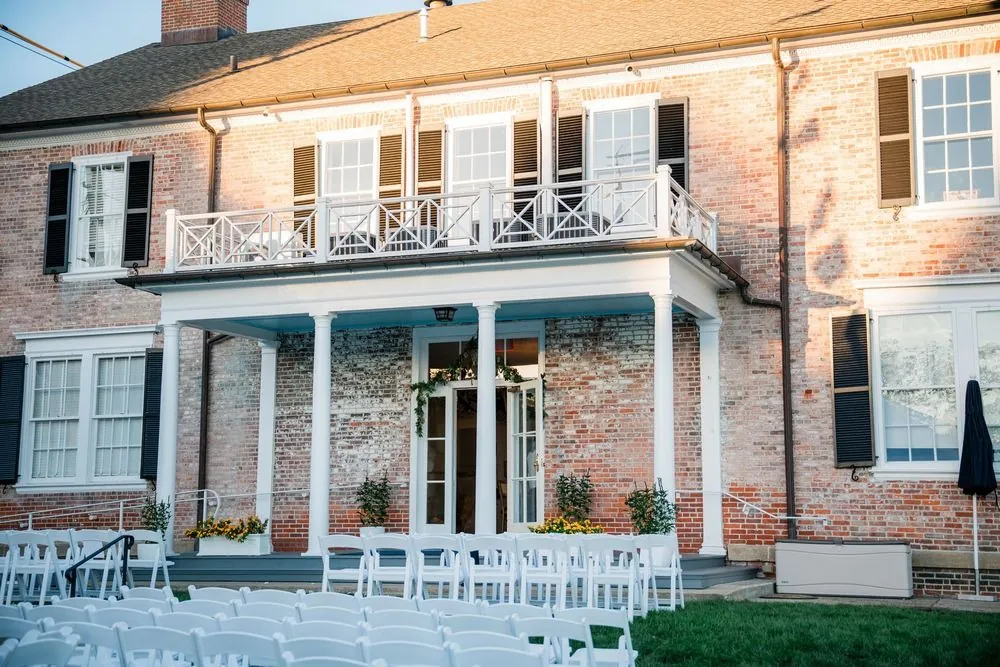 Brick clubhouse porch with white columns and rows of white chairs on the lawn