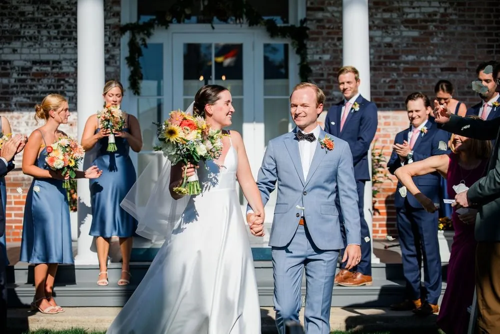 Isabelle and Bryce walk down the porch steps holding hands past bridesmaids in slate blue