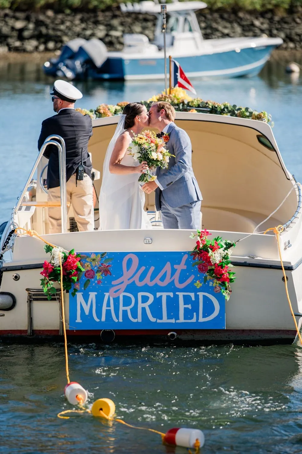 The couple kiss aboard a club launch with a Just Married sign on the stern