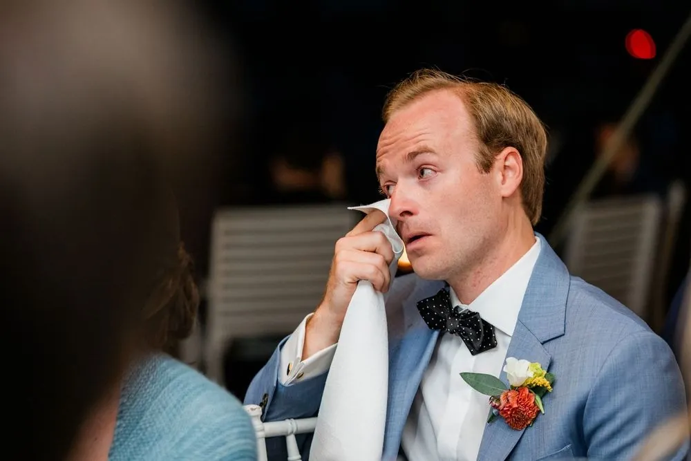 Groom wipes his eyes with a white napkin during the reception toasts