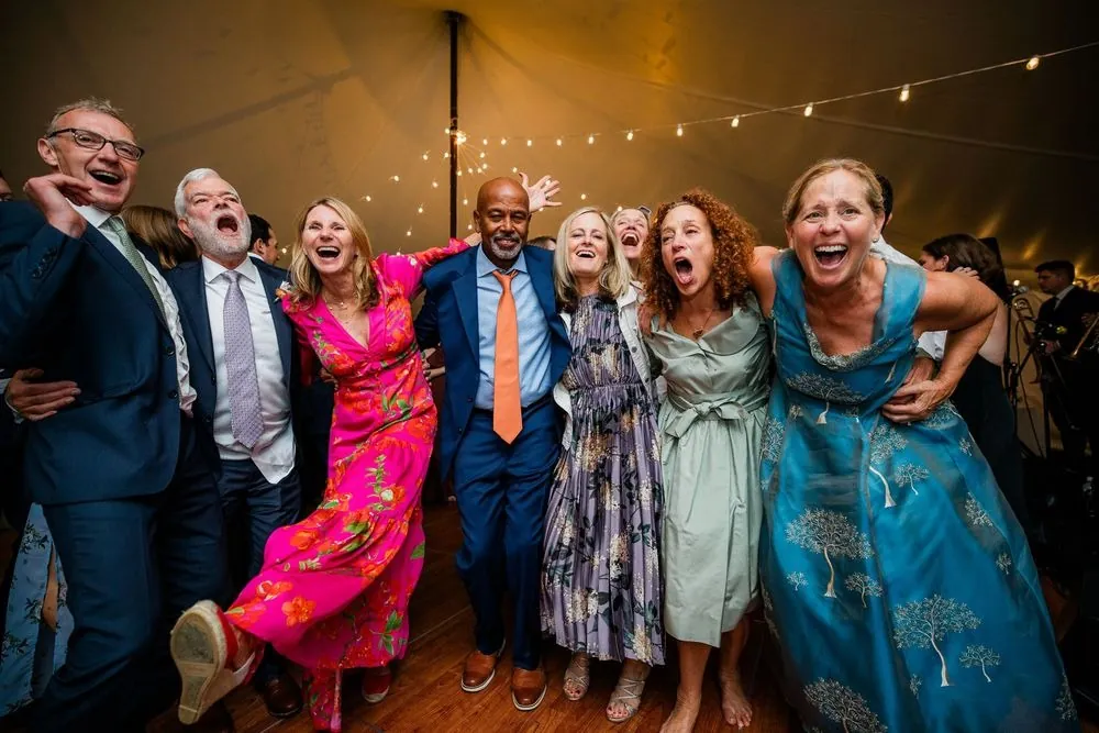 Guests in bright dresses and suits shout and pose together on the dance floor