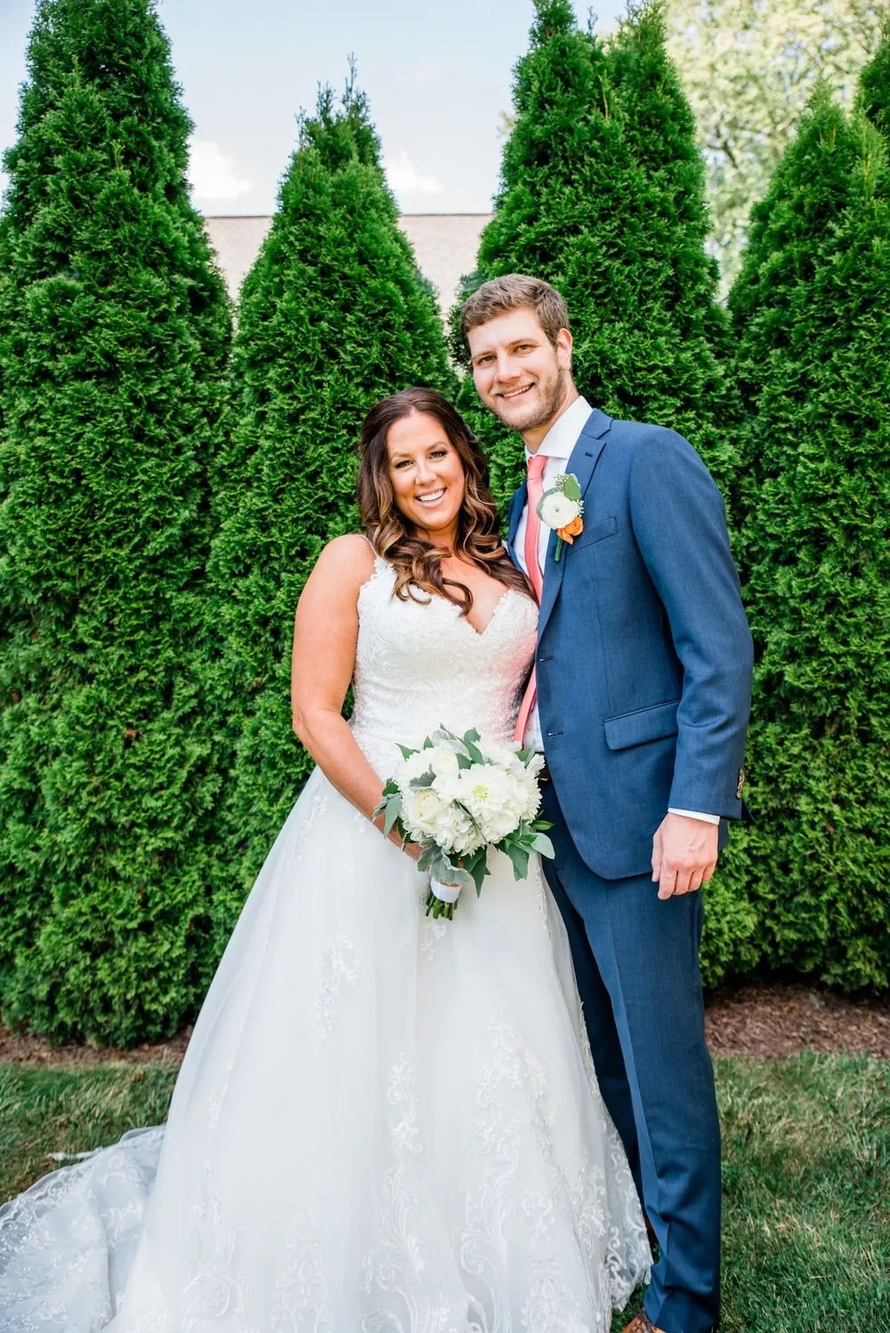 Jennifer and Stefan stand together in front of a row of tall arborvitae