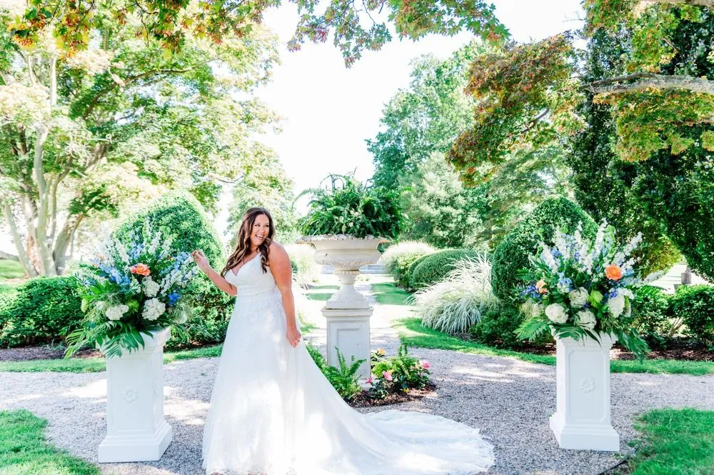 The bride stands alone on a garden path lined with white stone urns