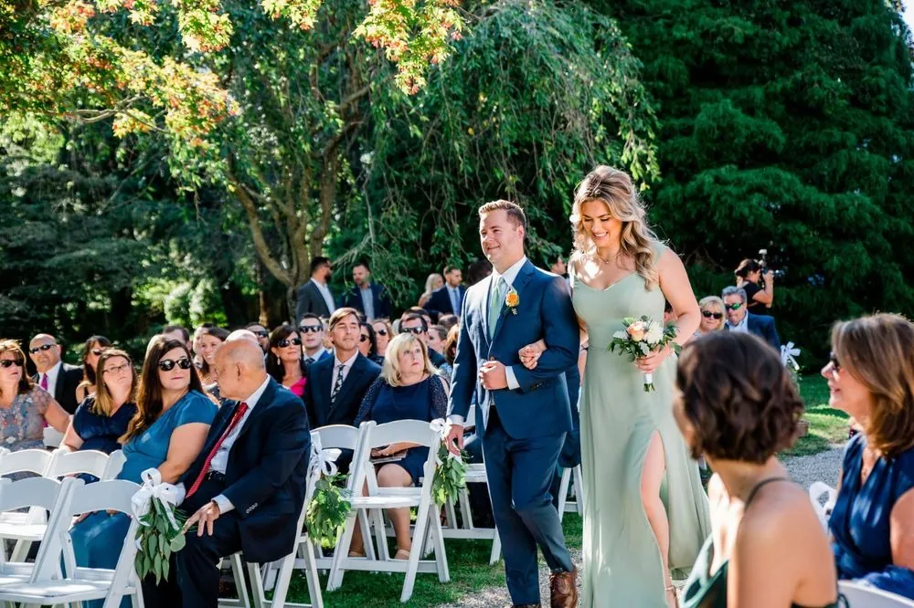 The bride walks down the aisle between guests seated on white chairs