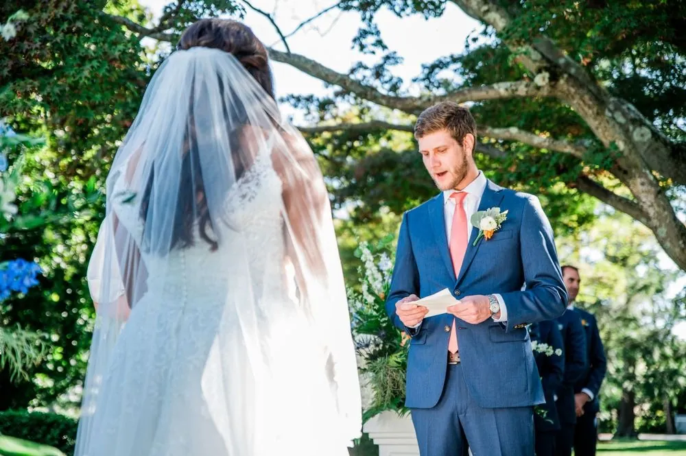 The groom reads his vows from a card as the bride looks on through her veil