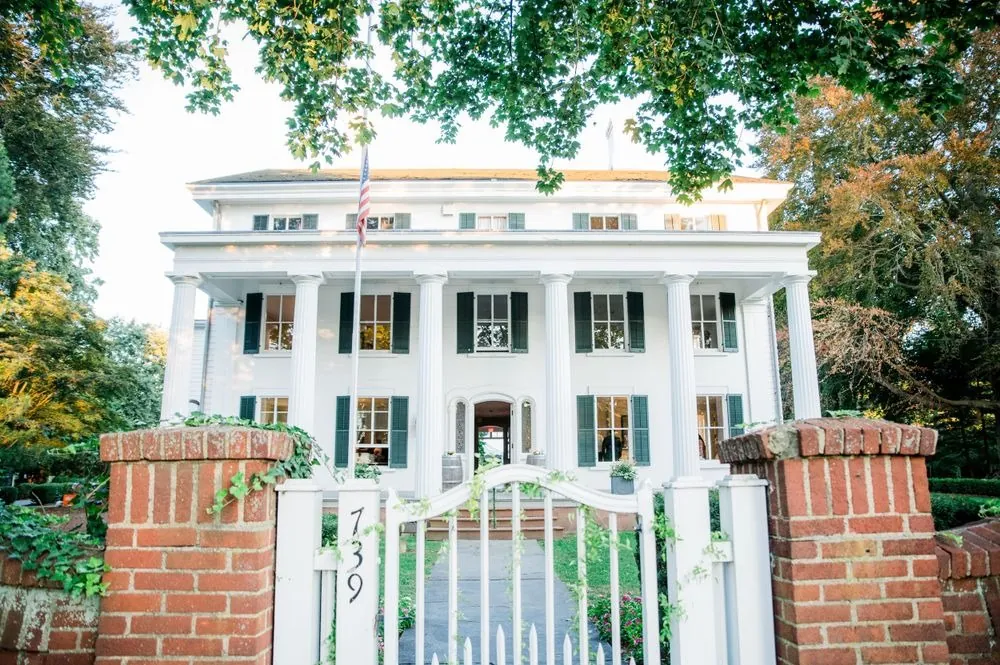 The white columned mansion behind a brick gate and garden walk