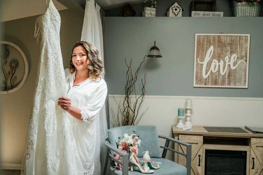 The bride smiles by her hanging gown in a pale blue room with a Love sign