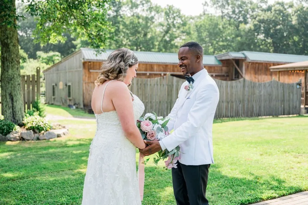 Jhamar and Tifany hold hands and laugh on the lawn in front of the barns