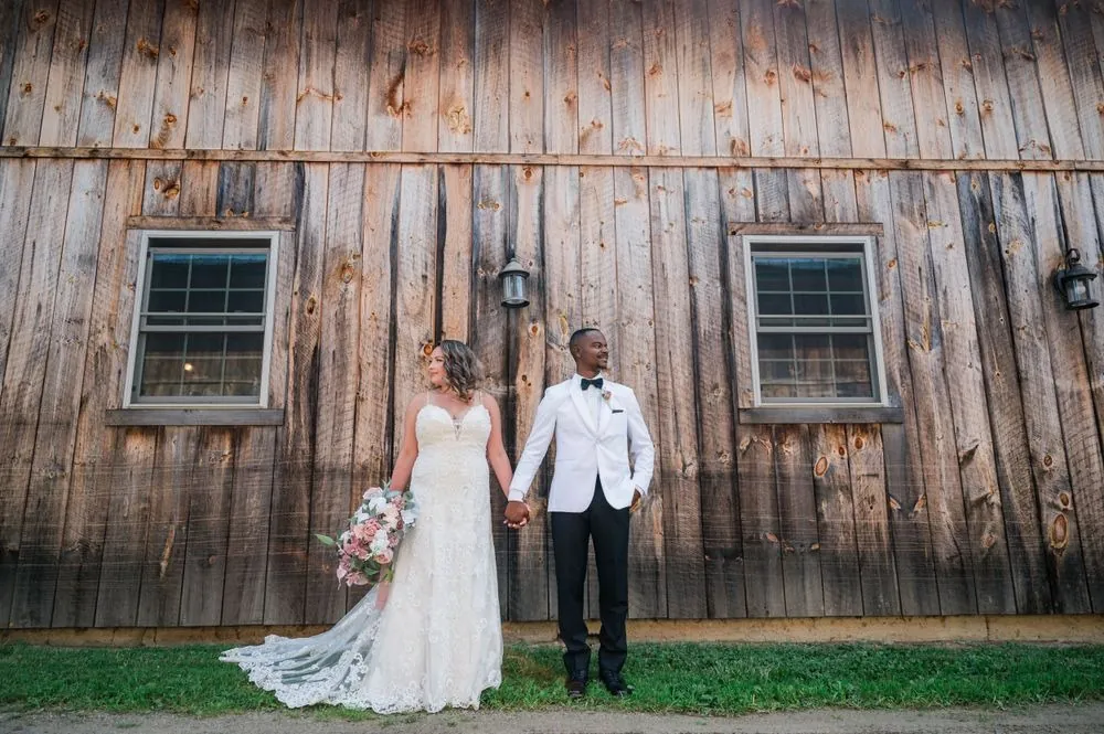 Jhamar and Tifany hold hands in front of a long weathered barn wall