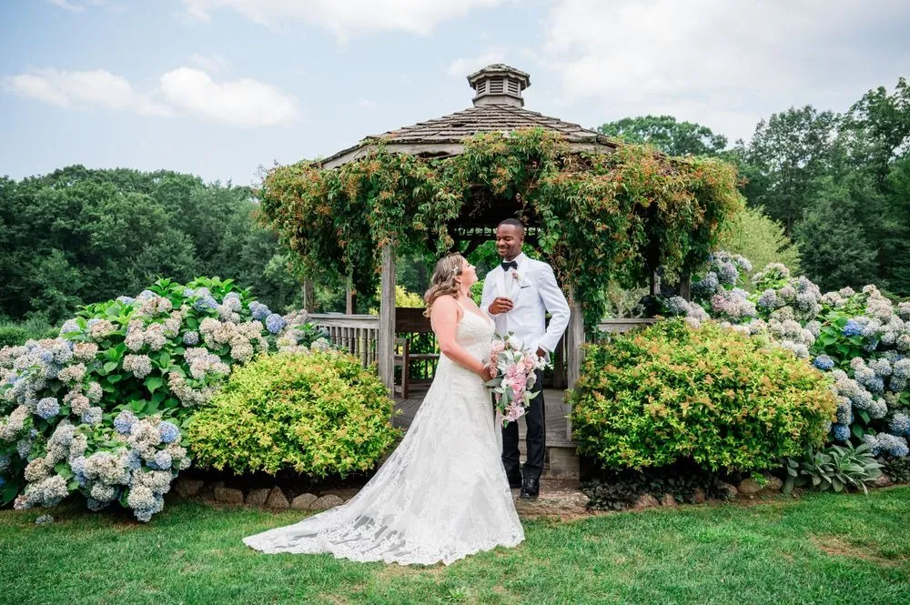 The couple embraces before a vine-covered gazebo ringed with hydrangeas