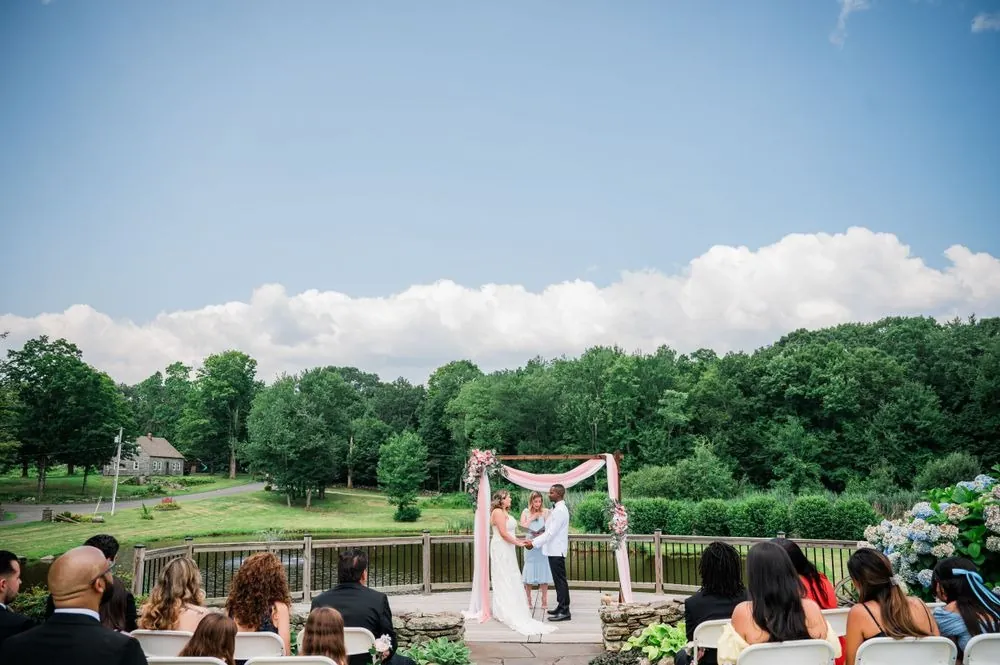Wide view of the ceremony at the arch with the pond and trees beyond