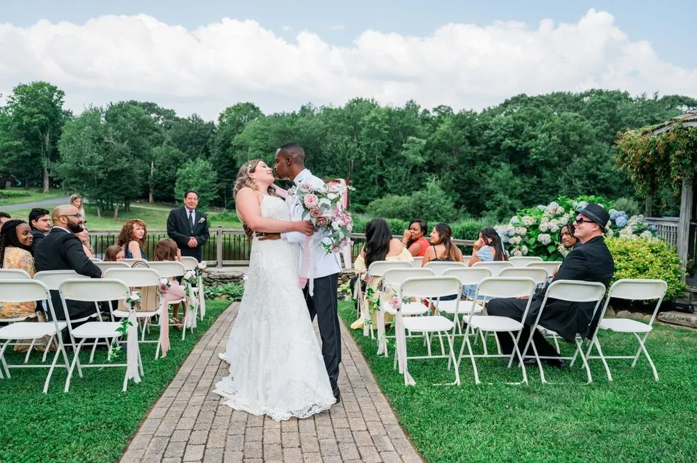 Jhamar and Tifany kiss in the middle of the brick aisle between white chairs