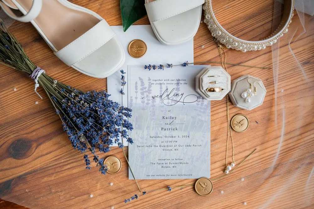 Invitation, ring box, bridal shoes and a bundle of dried lavender on a wood table