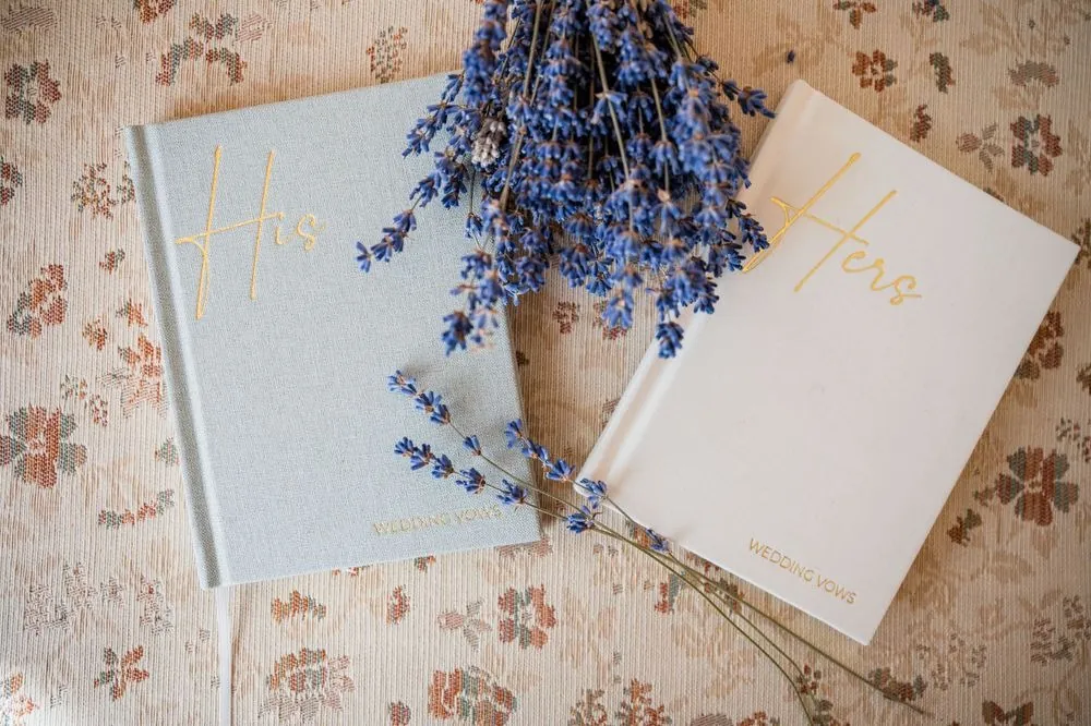 His and Hers vow books resting on a floral cloth under sprigs of lavender