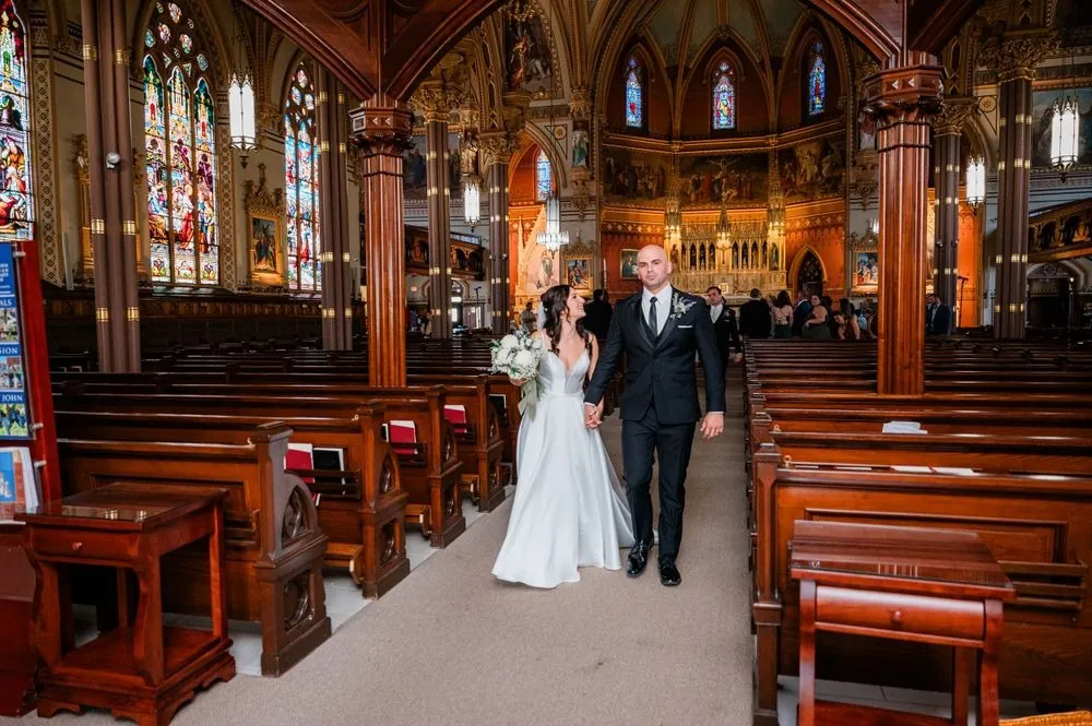 The bride walks down the church aisle on a man's arm between wooden pews