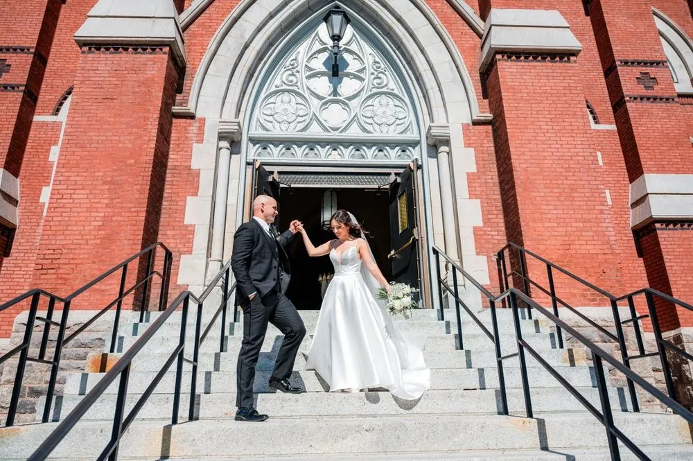 Kailey and Patrick come down the granite steps of a red brick Gothic church
