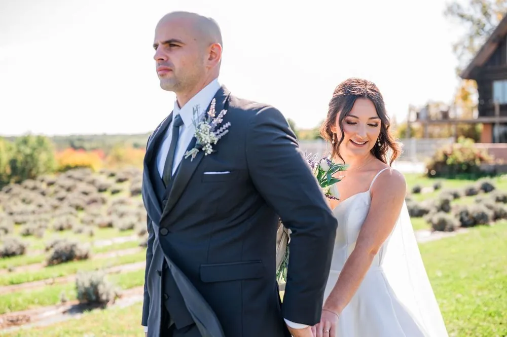 The groom looks off across the farm as the bride leans in smiling beside him