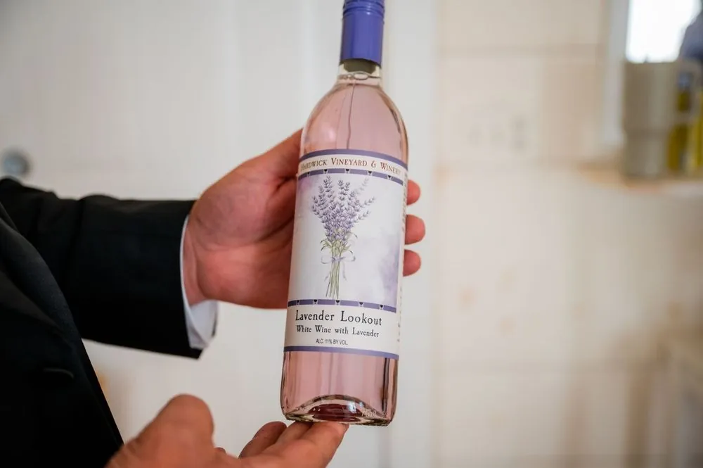 A hand holds a bottle of lavender-labeled rosé wine at the bar