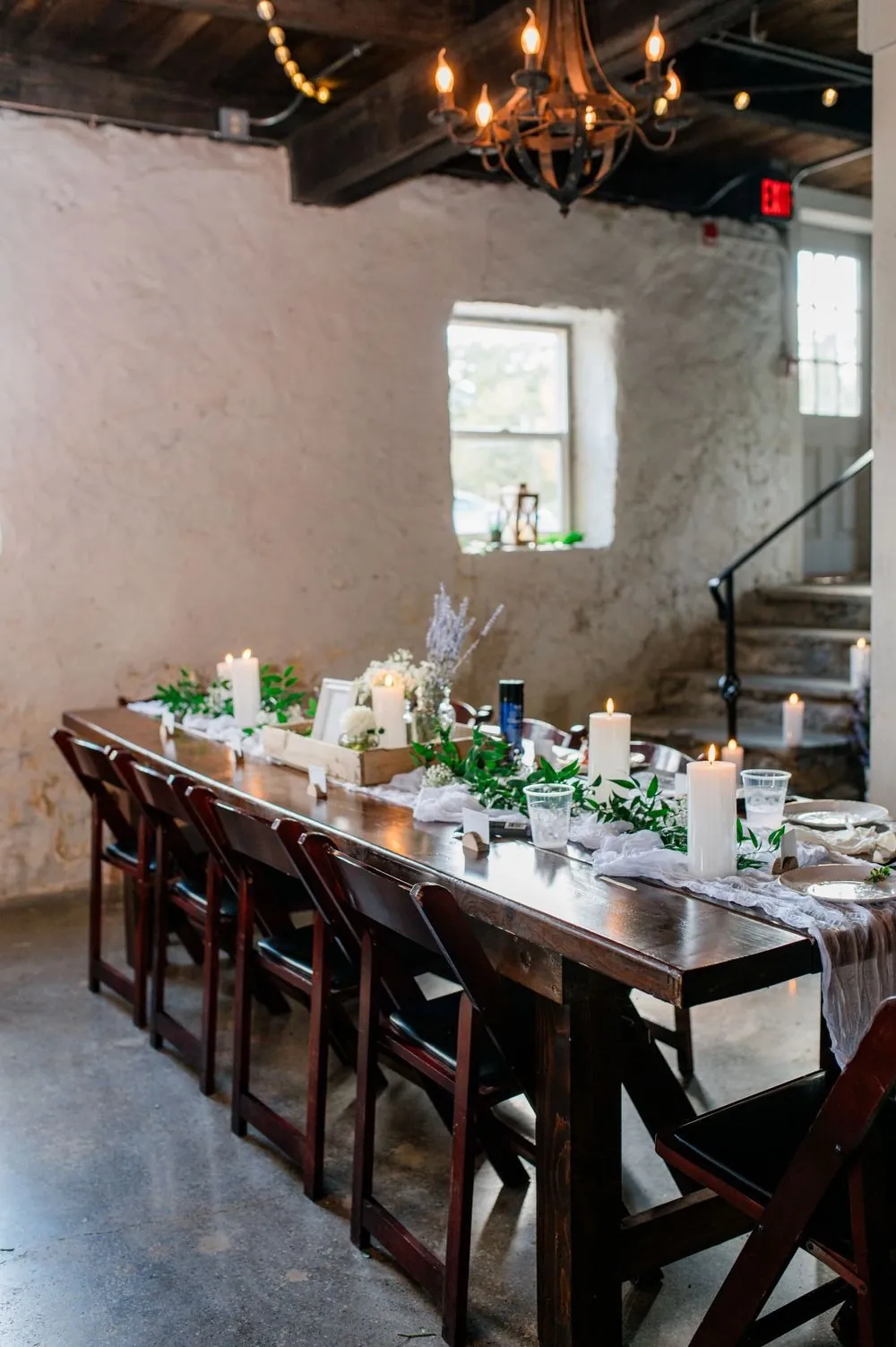 Long wooden reception tables set with greenery inside the farmhouse