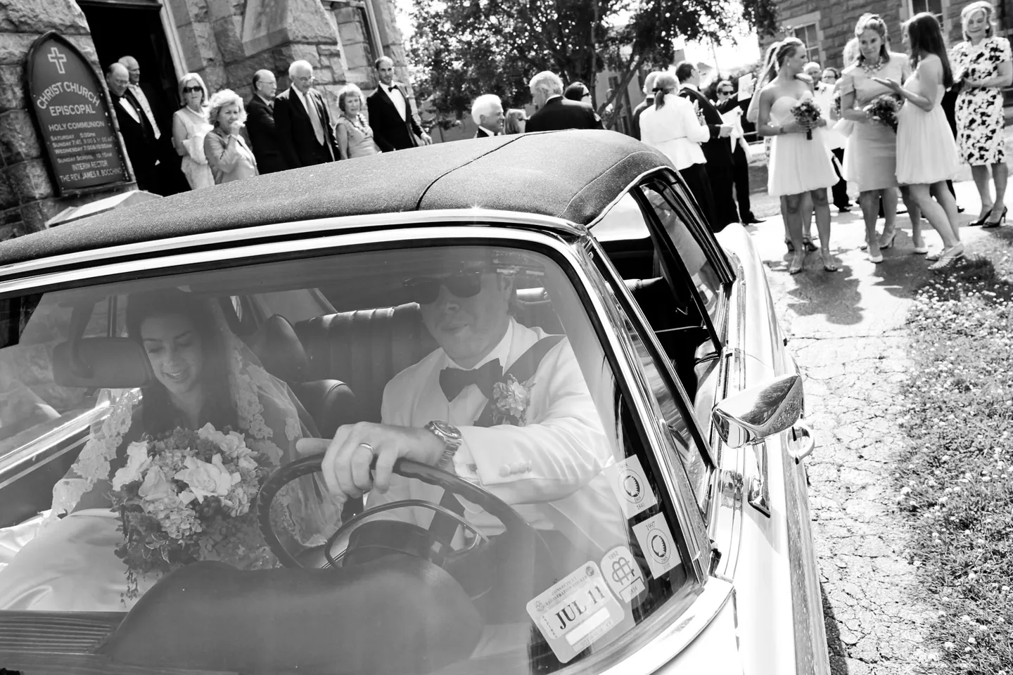 Black and white view through a vintage car window, Matthew driving and Kaitlin beside him